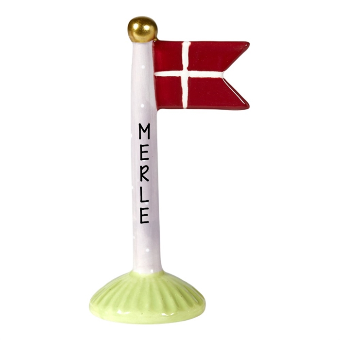 Keramisk flaggstång med röd flagga, vitt kors, vita prickar och namnet "MERLE" på stången.