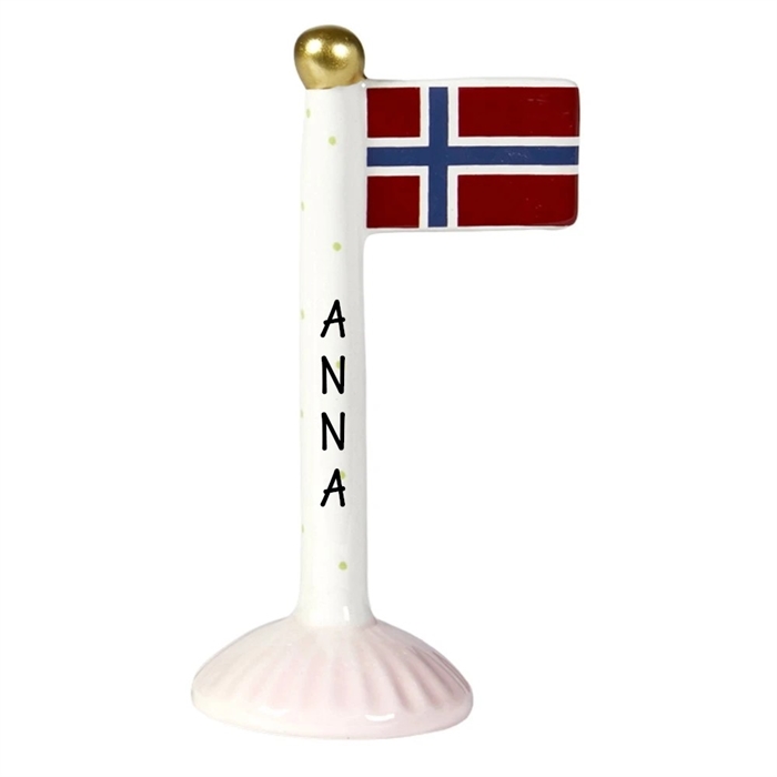 Keramisk flaggstång med norsk flagga, gyllene topp, prickar och namnet "ANNA" skrivet vertikalt.